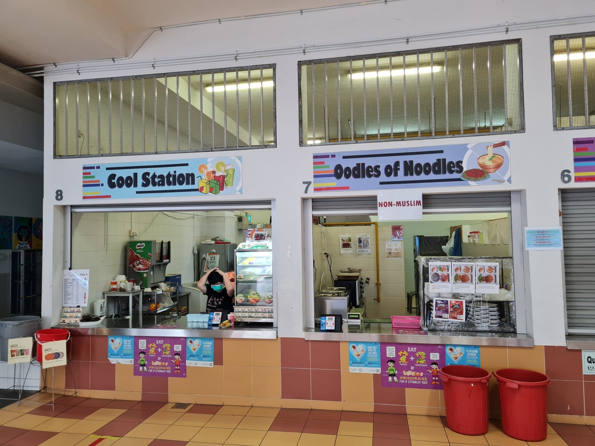 Two school canteen stalls labeled Cool Station and Oodles of Noodles with a masked worker visible inside.